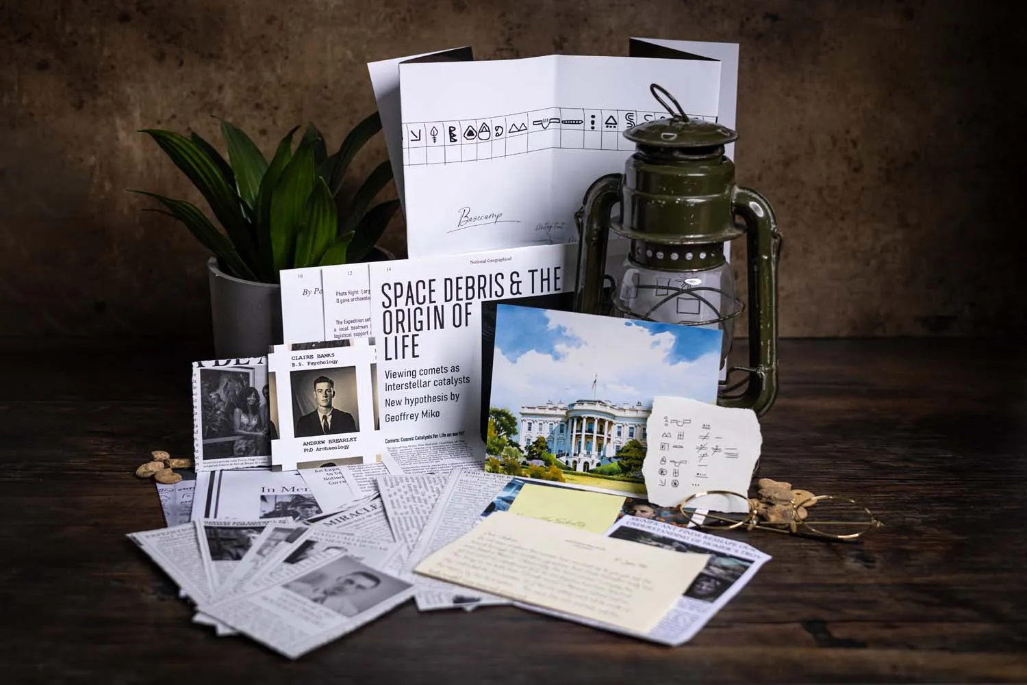 The Site Q case file laid out on a dark wooden table — National Geographic article, army-green hurricane lamp, Mayan glyphs and expedition correspondence